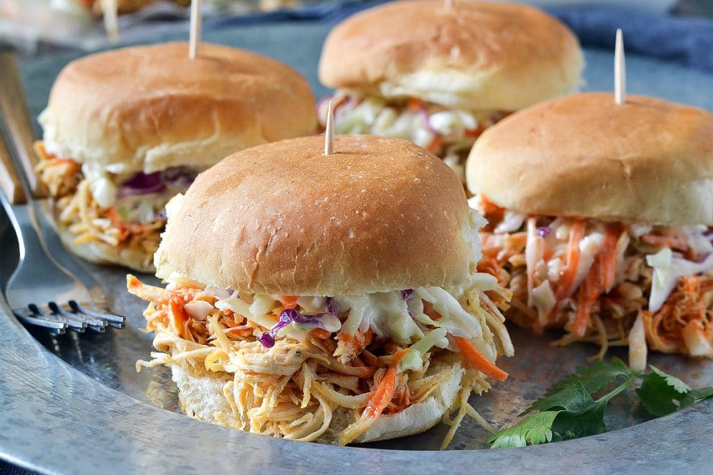4 shredded chicken sliders with cole slaw on a round metal plate with 2 forks