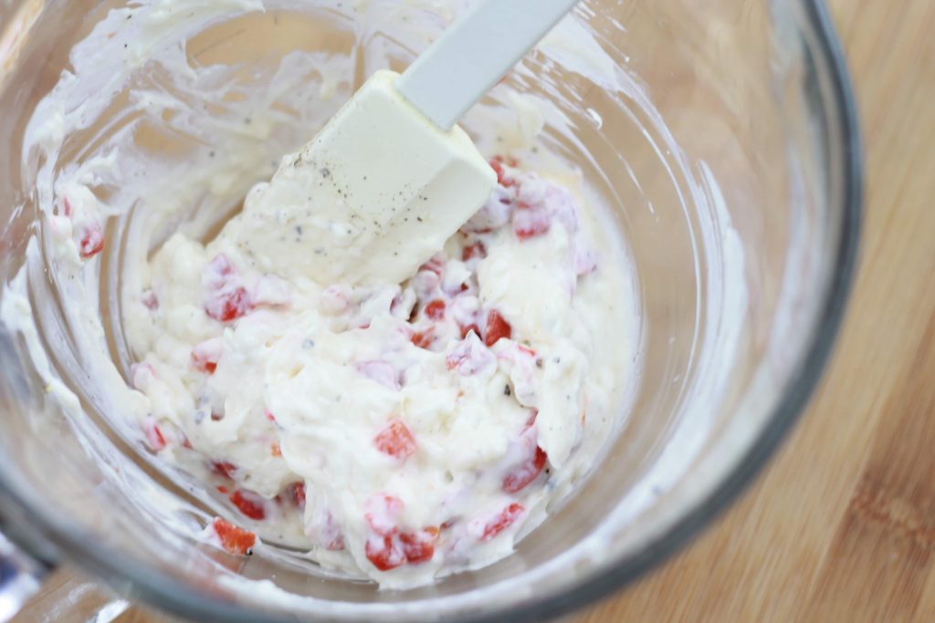 Cream cheese and diced tomatoes being mixed together in a clear mixing bowl.