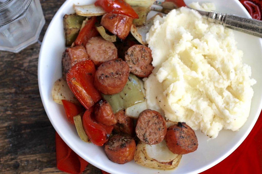 sausage, onions and peppers with mashed potatotes on a white serving plate.