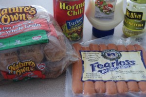 A package of whole grain hot dog buns, a package of hot dogs, a can of chili, a bottle of mayo and jar of pickles all placed on a counter ready to be prepped.