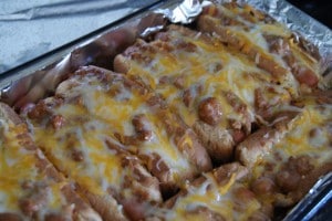 Oven toasted chili cheese dogs topped with melted shredded cheese on a baking sheet with foil.