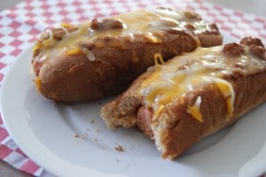 Two chili cheese coney hot dogs, topped with shredded cheese, served on a white plate.