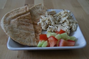 Pita bread served with shredded chicken and fresh cut fruit on a white plate.