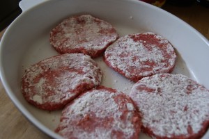 Five seasoned hamburger patties in a white dish ready to be cooked.