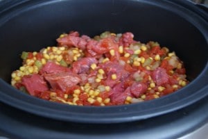A crockpot with beef, corn, and peppers, ready to be slow cooked into BBQ beef. 