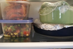 Prepped meals in plastic containers stacked and placed in a refrigerator. 