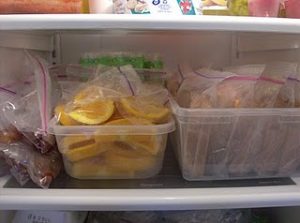 Two plastic bins one filled with bags of orange slices, the other with already made such sandwiches, ready for school lunch.