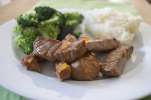 Orange teriyaki steak bites served on white plate with a side of broccoli and white rice.