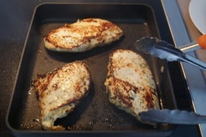Three cooked chicken breast on a baking sheet ready to be served with tongs.
