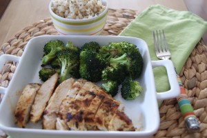 Lemon grilled dill chicken, served on a plate with a side of broccoli and a side cup of brown rice.