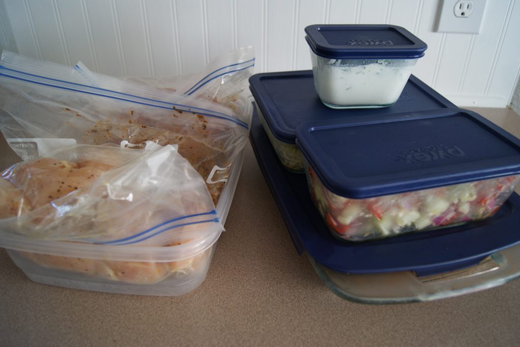 Prepped meals in glass storage containers ready to be stored, along side a plastic container with prepped meals in plastic zip lock baggies on a counter.