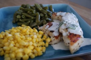 Cilantro cream chicken tenders served on a blue plate with a side of corn and green beans.