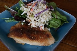 Blackened Tilapia served on a blue plate with a side salad topped with coleslaw.