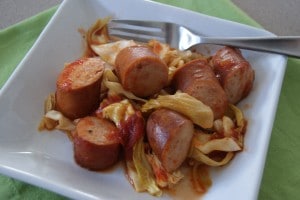 Sausage and cooked cabbage, served on a white plate.