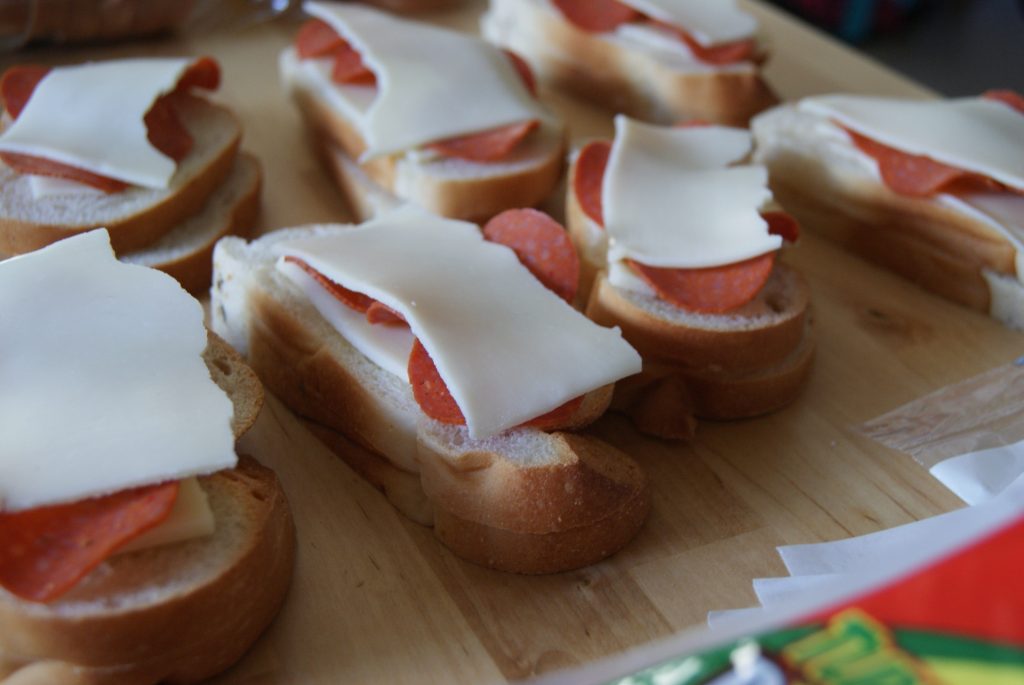 Asembly of French bread sandwiches with pepperoni and provolone cheese on a cutting board.