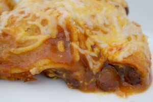 Bean and cheese enchilada topped with shredded cheese served on a plate.