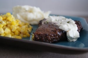 Balsamic steak topped with cream sauce served on a plate with a side of corn and mashed potatoes and gravy.