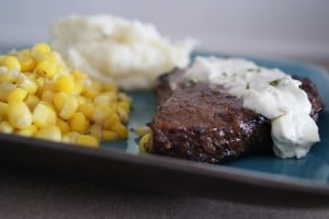 Balsamic steak topped with cream sauce served on a plate with a side of corn and mashed potatoes and gravy.