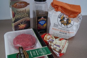 Beef broth, salisbury steak patties, with seasoning, flour and garlic on a counter.