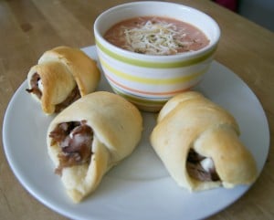 Three crescent rolls stuffed with ham served on a plate with a sup of soup.