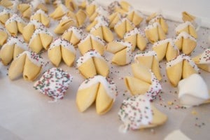 Many white chocolate covered fortune cookies placed on a baking sheet.