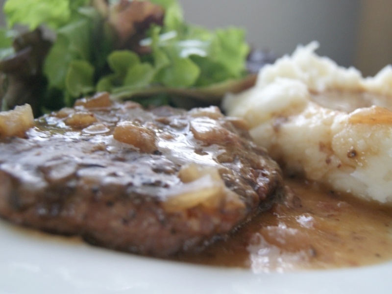 Salisbury steak with a brown mushroom gravy served with mashed potatoes and green salad on a white plate.