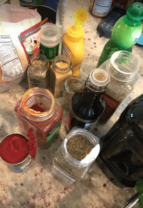 Opened containers of paprika, salt, pepper, bay leaves, mustards and oils for a dry rub to put on spicey steak bites.