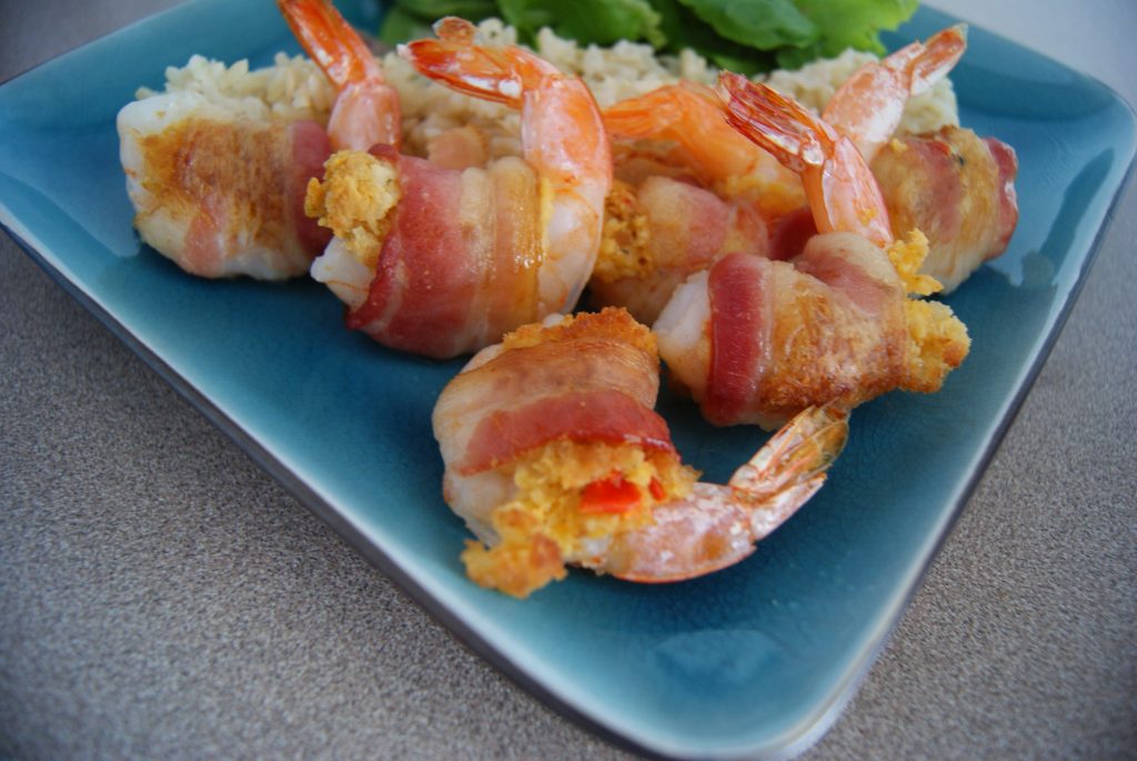Crab stuffed shrimp wrapped in bacon on a blue plate served with rice.