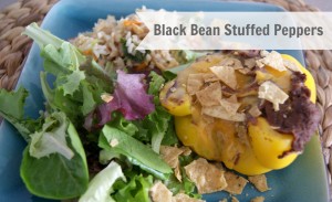 refried beens stuffed in yellow peppers on a blue dish with a side salad.