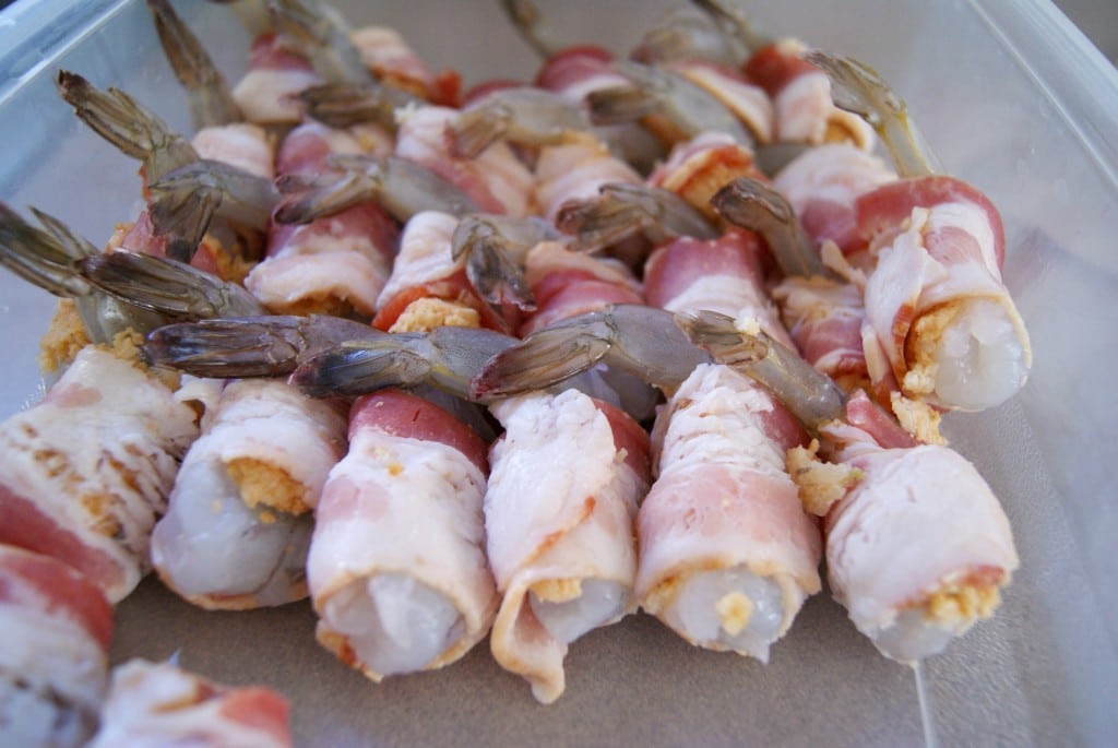 Raw shrimp with tails, wrapped in bacon stuffed with crab layered in a container.