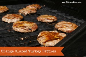 Orange glazed turkey patties cooking on an outdoor grill.
