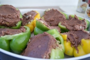 Green and yellow bell peppers stuffed with refried beans in a baking dish.