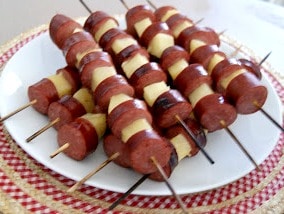 Nine sausage kebobs stacked and served on a plate.