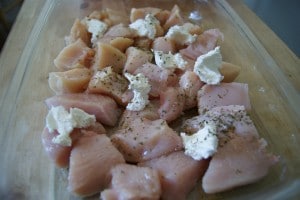 Chicken, with cream cheese and pepper in a clear baking dish.