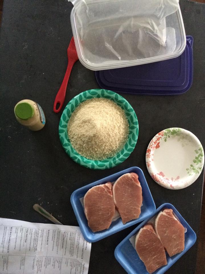 Four pork chops, a plate full of panko crumbs, and minced garlic, ready to be prepped for a meal.
