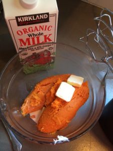 Two peeled sweet potatoes in a clear mixing bowl with butter and organic milk ready to be mixed together.