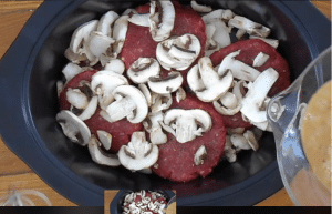 Hamburger patties with mushrooms and a bone broth mixture about to be poured from a glass bowl