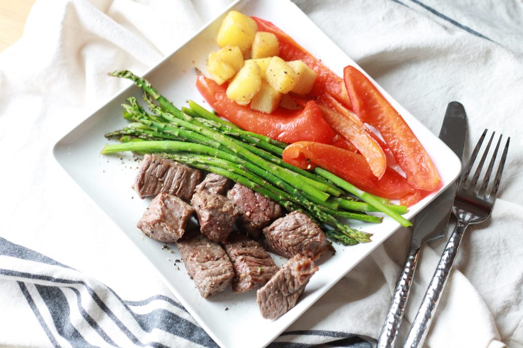 Asparagus, chopped pineapples, sliced red bell peppers, and steak all placed on a white plate ready to be eaten.