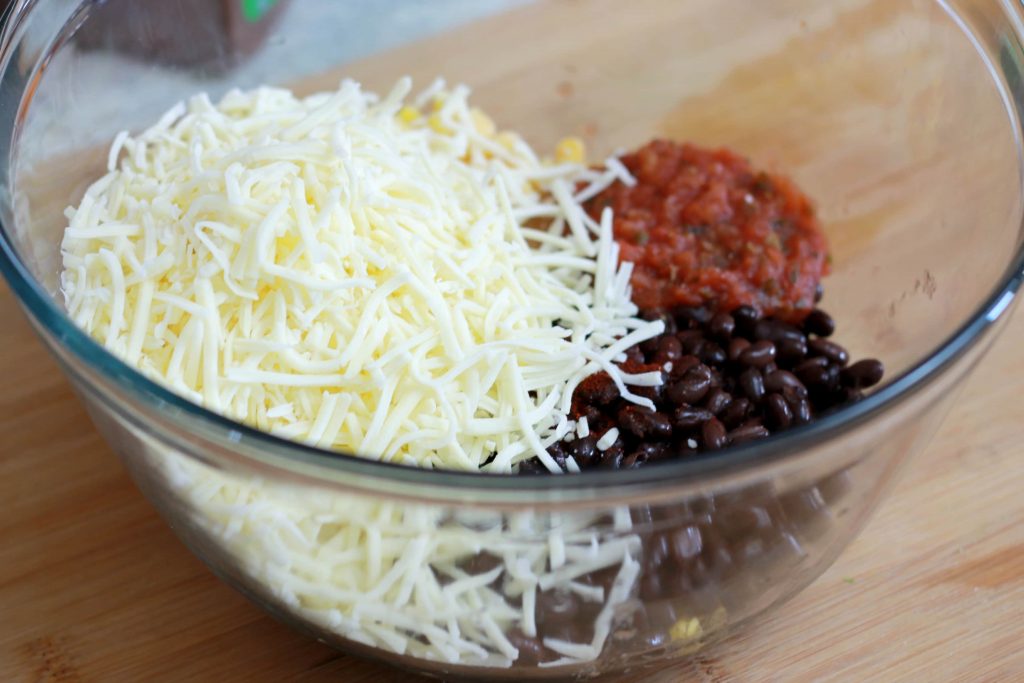 Black beans shredded cheese and salsa in a clear mixing bowl.