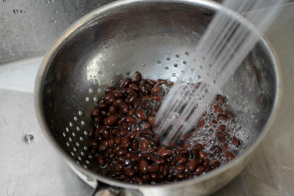 Black beans being rinsed by water in a colander.