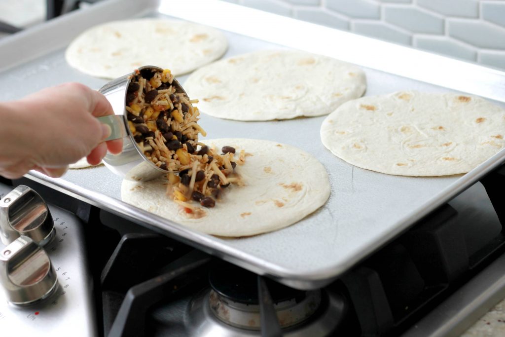 Black beans, shredded cheese, salsa, and corn getting added to the flour tortillas before being place in the oven.