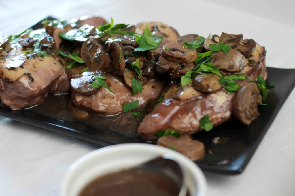 Cooked chicken topped with mushrooms and wine sauce topped with basil leaves served on a plate with a smile side of mushrooms.