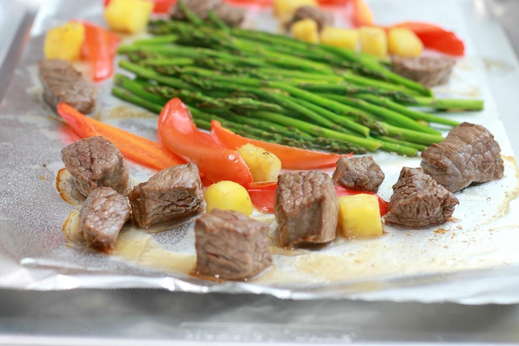 Asparagus, chopped pineapples, sliced red bell peppers, and steak all placed on one pan ready.