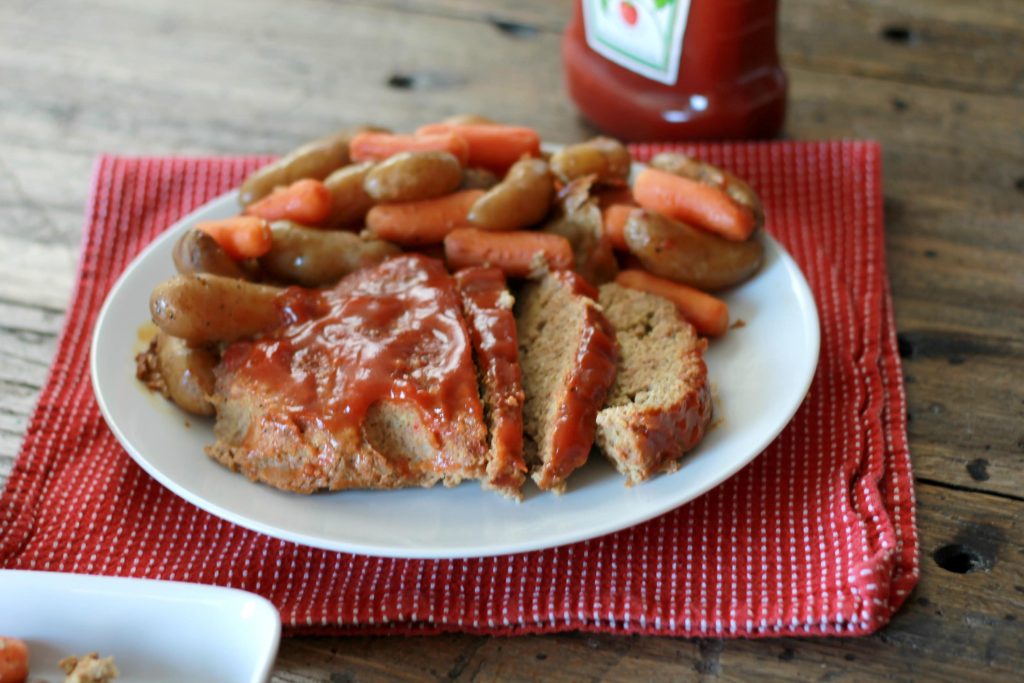 Meatloaf served on a plate with a side of slow cooked vegetables, topped with ketchup.