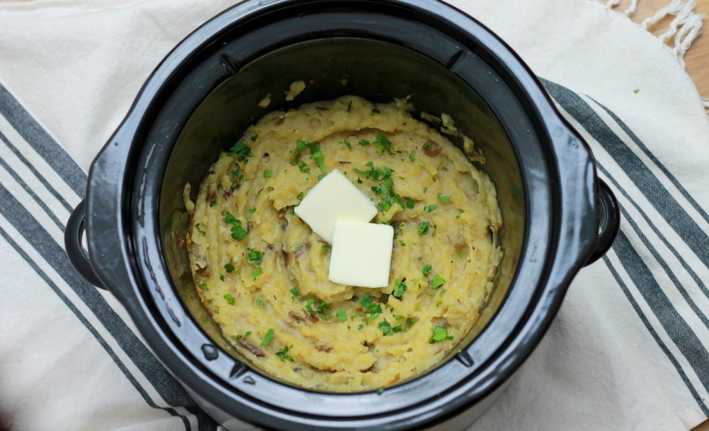 Mashed potatoes in the crockpot, whipped and topped with two slices of butter and seasoning.