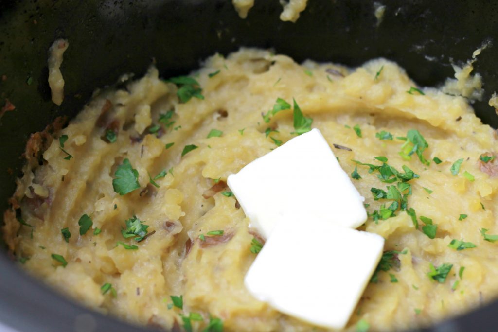 Mashed potatoes in the crockpot, whipped and topped with two slices of butter and seasoning.