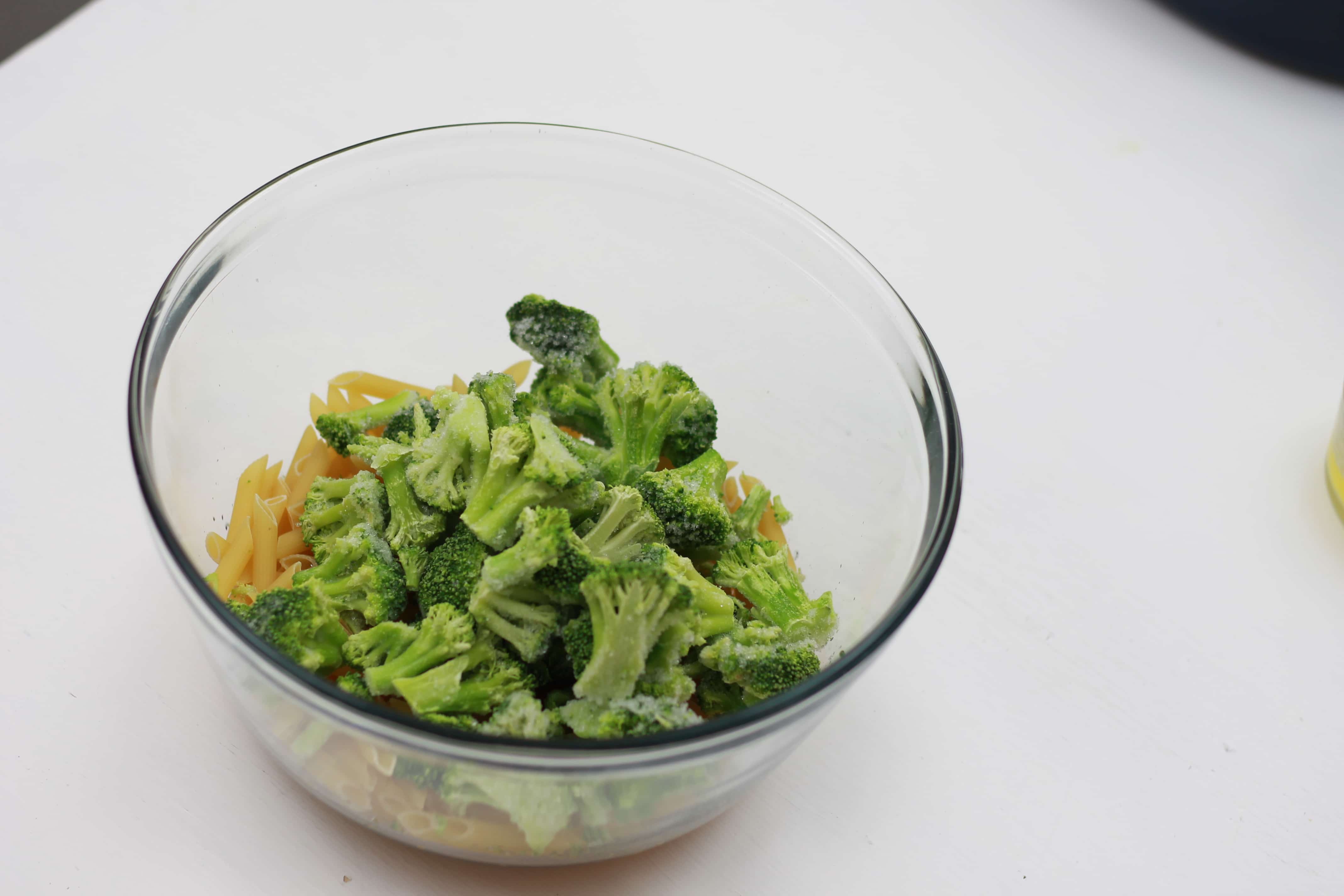 Frozen broccoli, and shredded cheese in a clear bowl.