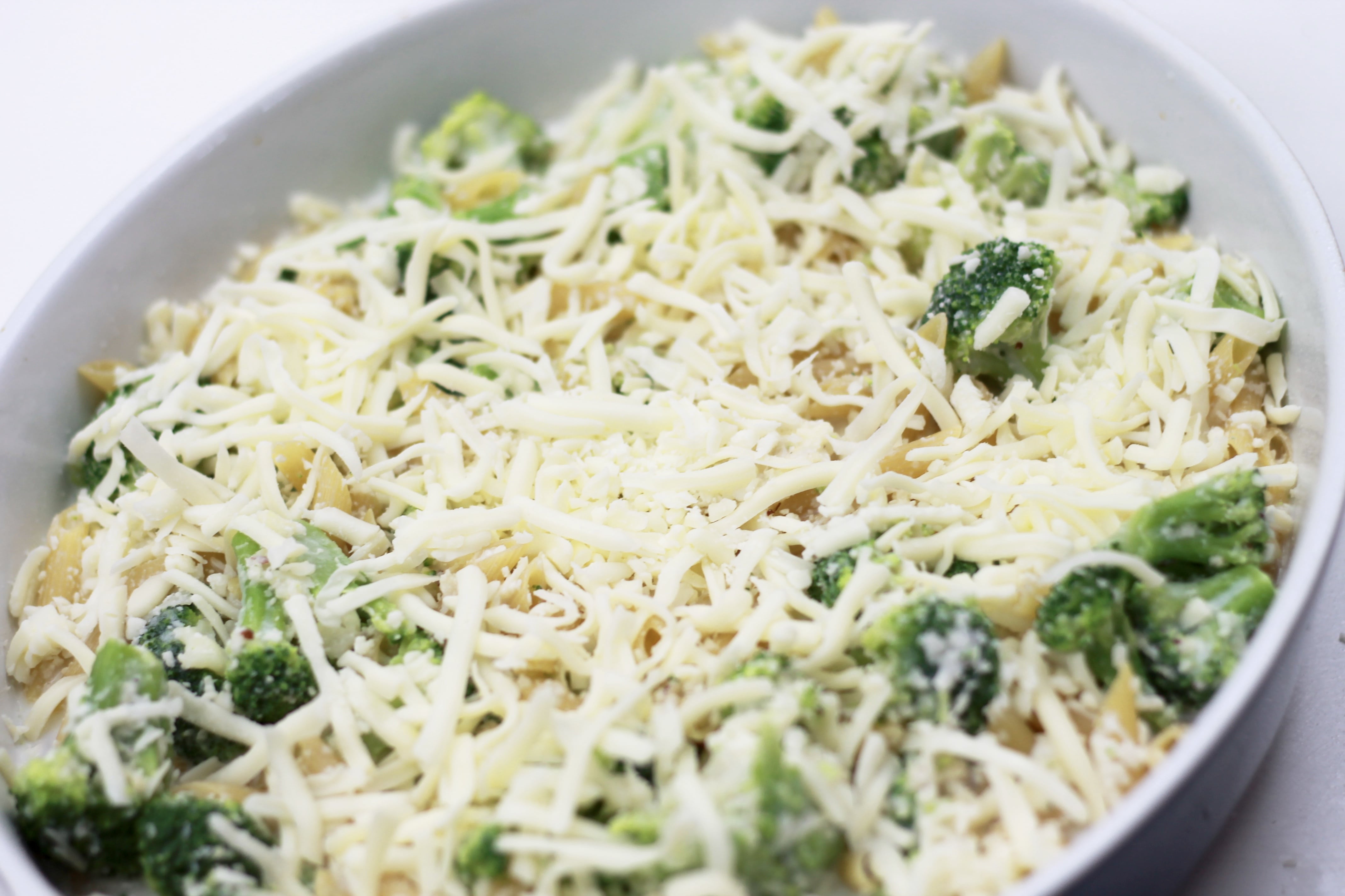 Cooked broccoli, pasta, and shredded cheese in a dish ready to be served topped with more cheese.
