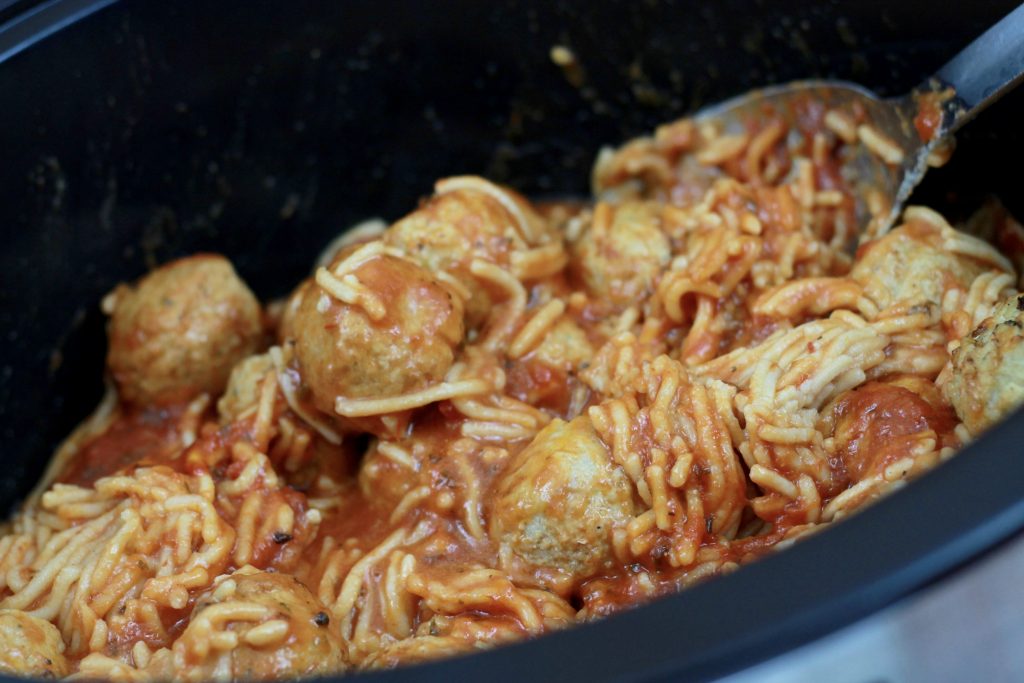 Cooked gluten free multi grain spaghetti pasta with sauce and meatballs in a crockpot.