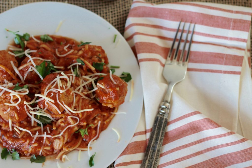 Gluten free multi grain spaghetti pasta with sauce and meatballs served with shredded cheese on a plate ready to be eaten.